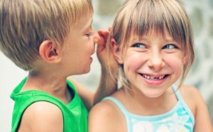 Un bambino parla all'orecchio di una bambina